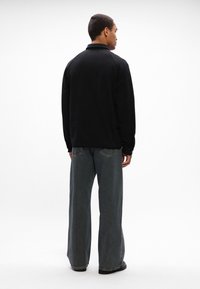 Casaco de fleece preto com colarinho, visto pelas costas. Combinado com jeans de ganga escuros de pernas largas. Design simples e limpo, sem detalhes adicionais.