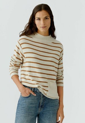 Cremefarbener Pullover mit braunen Querstreifen, hohem Kragen und Fronttasche, kombiniert mit blauen Jeans. Weicher Stoff und lockere Passform.