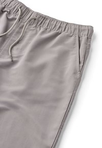 Pantalon décontracté gris clair avec taille élastique et cordon de serrage, doté de poches latérales et d'une texture de tissu lisse.