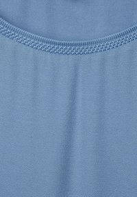 Vaaliharmaa kangas, jossa on pehmeä, rakenteellinen pinta. Pyöreä kaula-aukko sisältää monimutkaista ompelua reunoilla, mikä parantaa suunnittelua.