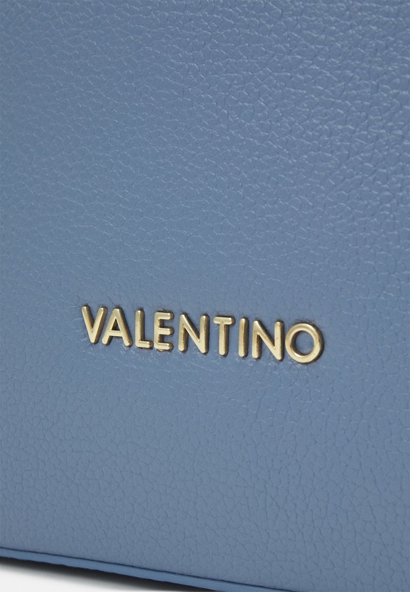 Lichtblauwe leren tas met een gestructureerde afwerking. Gouden "VALENTINO" logo elegant op de voorkant gedrukt, wat de merkidentiteit benadrukt.