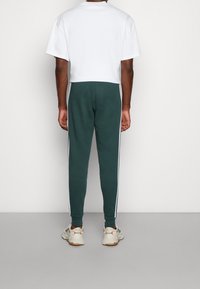 Gröna joggers med vita sidostripes, i kombination med en kortärmad vit t-shirt. Tyget verkar mjukt, med en avslappnad passform och slät textur.