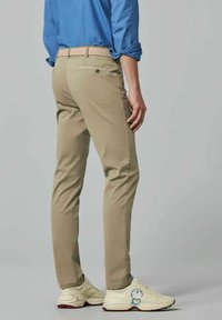 Beige chinos met een slim fit, voorzien van een geweven tan riem, achterzak met knoop, gecombineerd met crèmewitte sneakers met een cartoonfiguur.