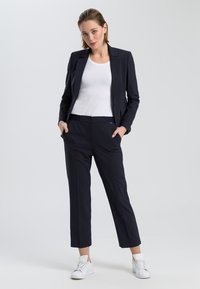 Navy blazer with matching tailored trousers, made from smooth fabric; paired with a white tank top and white sneakers.
