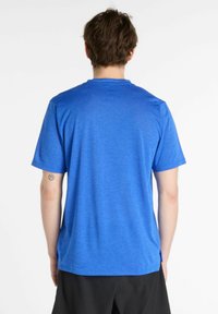 T-shirt bleu à manches courtes en tissu texturé, avec un col rond et des fentes sur les côtés pour faciliter le mouvement. Vue arrière montrée.