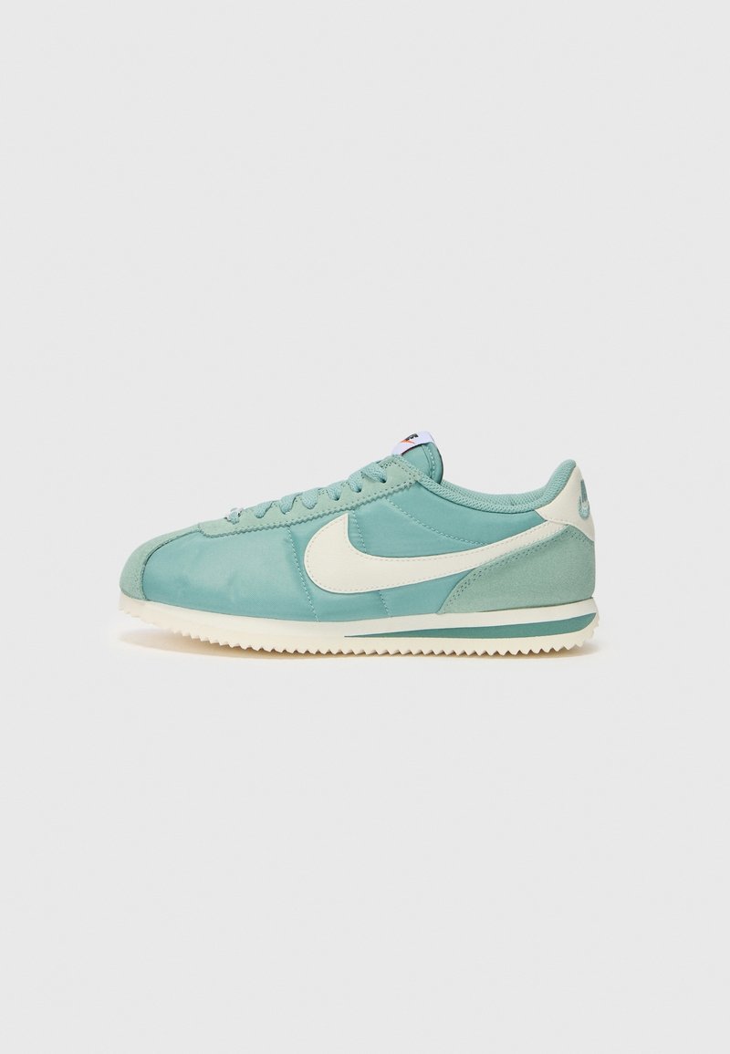 Baskets Nike Cortez bleu sarcelle clair avec logo swoosh blanc, semelle blanche et design à lacets sur fond gris clair uni.