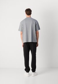 Grå t-skjorte med korte ermer og rett snitt, brukt med svarte joggebukser og hvite sneakers. Bakfra vises et enkelt design og en avslappet passform.