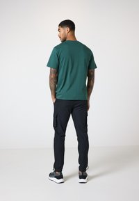 Grønn t-skjorte med korte ermer, bomullsmateriale, rund hals, kombinert med sorte cargo-bukser med sidelommer og sorte sneakers med hvite såler.