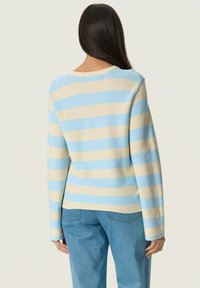 Stribet sweater med skiftevis lyseblå og beige farver, ribbet tekstur, rund halsudskæring og lange ærmer, parret med lyseblå jeans.