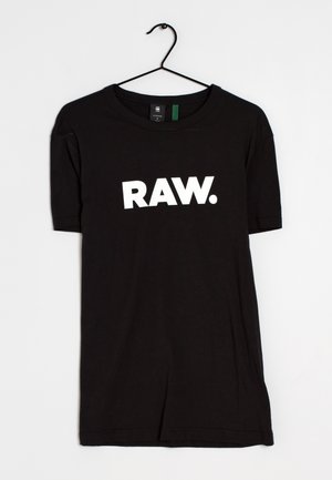 Black short-sleeve T-shirt hanging on a hook with bold white text "RAW." printed across the chest on a plain background.