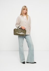Zielona syntetyczna torba na ramię z metaliczną gwiazdką, górnymi uchwytami i błyszczącym wykończeniem. W połączeniu z luźnymi jasnoniebieskimi dżinsami oraz beżową koszulą na guziki.