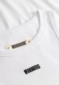 Débardeur blanc à côtes avec logo "WOODBIRD" noir brodé sur le devant et étiquette assortie à l'intérieur du col.