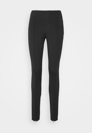Schwarze Slim-Fit-Hose mit hoher Taille und Reißverschlüssen am Knöchel, gezeigt vor einem einfachen hellen Hintergrund.