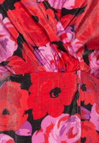 Bloemige stof met grote rode, roze en paarse bloemen op een zwarte achtergrond. Het materiaal heeft een lichte glans en is geplooid bij de taille.