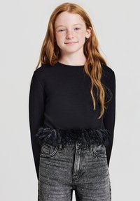 Maglietta nera a maniche lunghe con orlo in finta pelliccia nera testurizzata, abbinata a jeans grigi scuri con un sottile motivo a puntini.