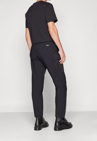 Svart t-shirt med korta ärmar som kombineras med svarta smala byxor med cargofickor och en texturerad yta, bärs med svarta stövlar.