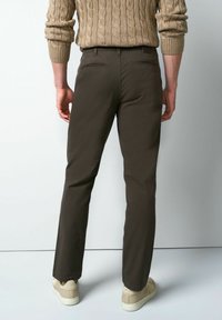 Bruine broek met patroon en een slanke pasvorm, twee achterzakken en een gladde textuur, gecombineerd met beige sneakers en een gebreide beige trui.
