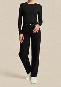 Pantaloni neri a vita alta con gambe dritte, abbinati a un top nero a manica lunga aderente. La modella indossa scarpe bianche slip-on. Tessuto dalla texture liscia.