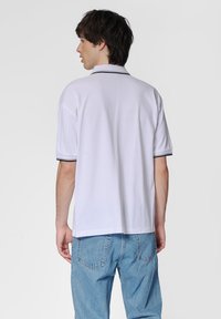 Witte polo met korte mouwen, met een zwarte bies op de kraag en mouwen. Draag het met lichtblauwe spijkerbroek.