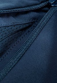 Granatowy materiał o gładkiej teksturze i delikatnym połysku, z zamkiem błyskawicznym oraz siateczkowymi detalami wzdłuż szwu.