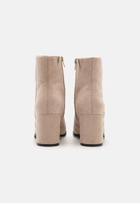 Bottines en daim beige avec bout rond, talon bloc et fermeture éclair. Texture lisse avec un design simple et épuré.