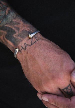 Silver metal cuff bracelet with two gold accents, featuring a smooth texture and a minimalist, curved design, worn on a tattooed wrist.