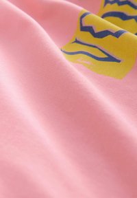 Růžová látka se žlutým a modrým grafickým potiskem, s jemnými sklady a hladkou texturou zblízka.