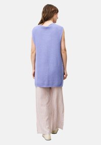 Ärmelloses, lavendelfarbenes Stricktop mit strukturiertem Muster, kombiniert mit breiten, gestreiften Hosen in sanften Farben und neutralem Schuhwerk.
