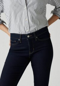 Mörkblå denimjeans med hög midja, kontrasterande sömmar och framfickor, matchade med en randig skjorta med knäppning.