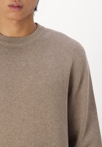 Pulover tricotat maro cu decolteu rotund. Materialul pare moale și ușor texturat, având o culoare uniformă fără modele.