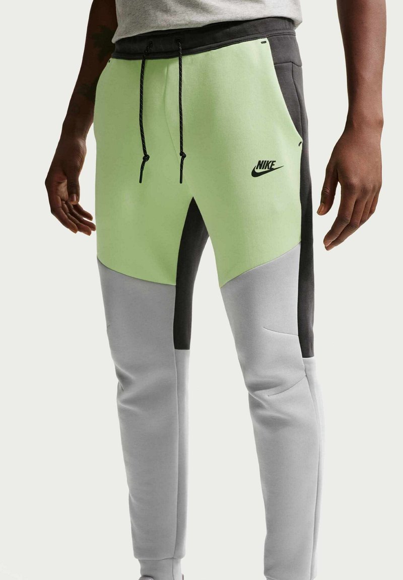 Mand iført Nike løbebukser i blokfarver i lysegrøn, grå og sort med snøre i taljen og sidelommer.