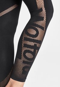 Svart åtsittande tränings topp med meshdetaljer längs ärmen, dekorerad med kontrasterande stor text i svart. Slätt tyg och texturdetaljer.