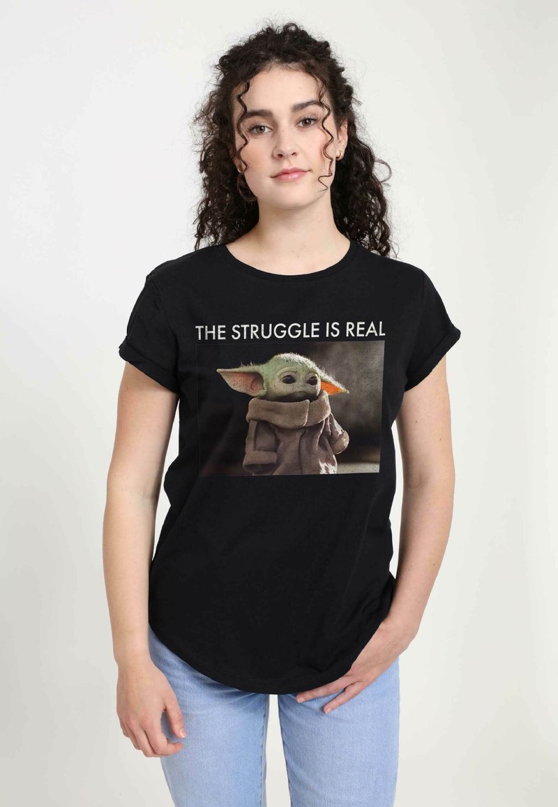 Camiseta de algodón negra con una imagen a color de un personaje con orejas grandes, con el texto "LA LUCHA ES REAL" en blanco arriba.