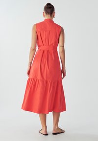 Korale obleko brez rokavov midi dolžine z večplastno krilom, pasom in ovratnikom s gumbi. Narejena iz lahkega blaga z gladko teksturo.