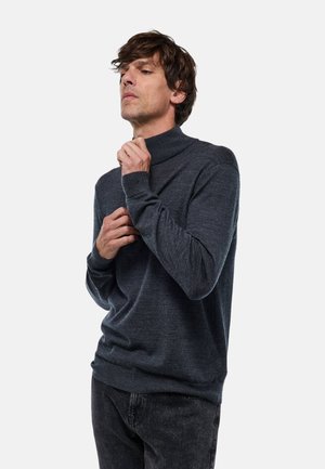 Pull en col roulé gris foncé en tricot doux, avec des poignets côtelés et une coupe décontractée, porté avec un jean noir.