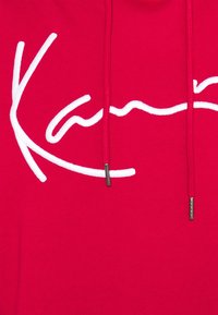 Sudadera roja brillante con el logo de la marca bordado en cursiva blanca en la parte frontal y cordones rojos a juego con puntas metálicas.