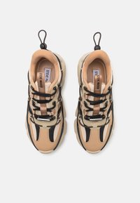 Zapatillas chunky en beige y negro, que presentan una parte superior de malla, cordones integrados y una suela de goma con acentos sutiles.