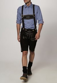 Traditionele Beierse outfit met een blauw-wit geruit overhemd en bruine lederhosen met decoratieve borduursels en bretels.