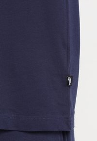 Mörkblå bomullströja med rund halsringning, korta ärmar och en liten svart Puma-logotags vid fållen. Mjuk textur.