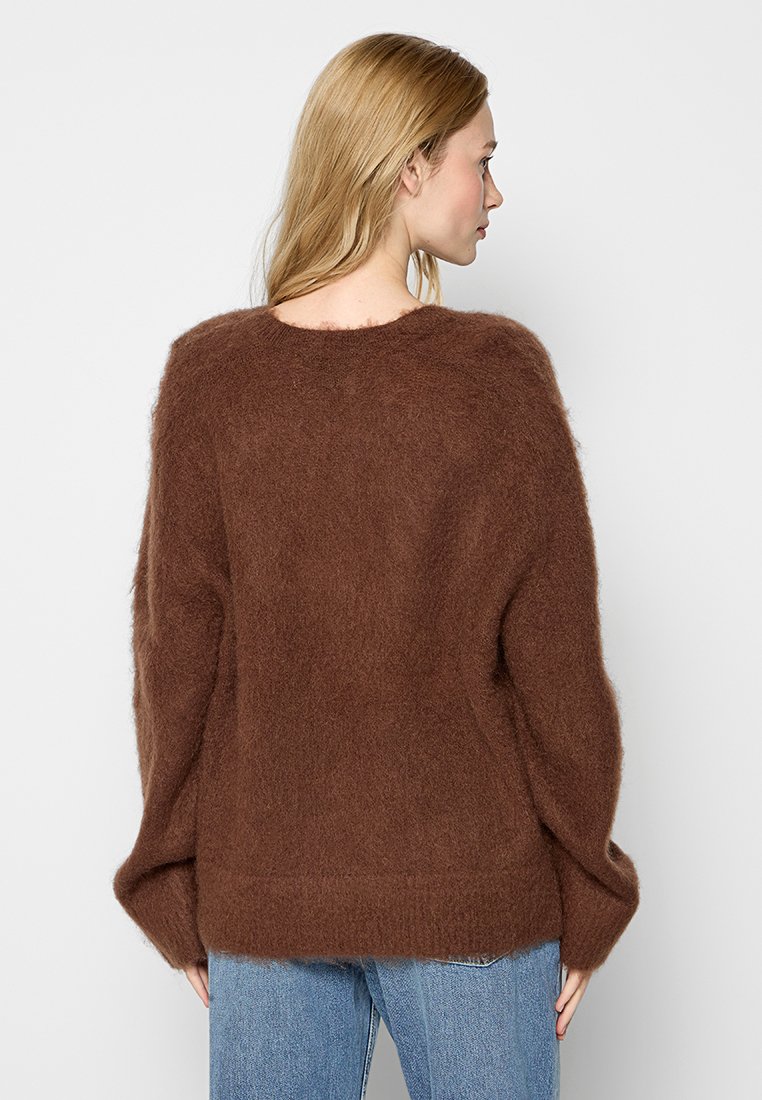 Un pull en tricot surdimensionné marron avec une texture douce, un col rond et des épaules tombantes. Associé à un jean en denim bleu clair.