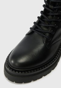 Bottine en cuir noir avec bout rond, semelle texturée et lacets noirs. Présente des coutures minimales et une semelle extérieure robuste en caoutchouc géométrique.