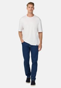 Bílý tričko s krátkým rukávem a volným střihem, v kombinaci s tmavě modrými džínami a námořnickými teniskami. Jednoduchý design, žádné vzory nebo loga.