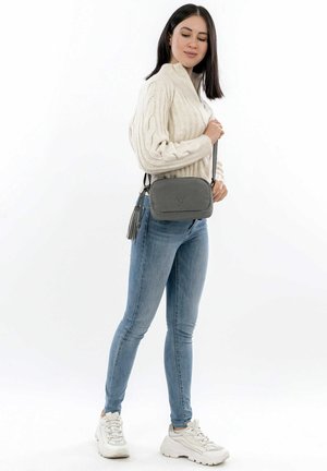 Borsa a tracolla grigia realizzata in materiale testurizzato, con un accento di frangia e un logo sottile. Indossata da una persona in abbigliamento casual.