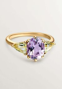 Anillo de oro con una piedra ovalada lila central rodeada de dos piedras en forma de pera de color verde claro, engastadas con acentos de garras.