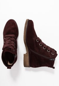 Bordowe zamszowe botki za kostkę z zaokrąglonym noskiem, sznurowane z przodu i zamkiem po boku. Posiadają fakturowaną brązową gumową podeszwę i metalowe przelotki na sznurówki.