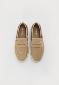 Barna suede anyagú slip-on cipők, párnázott gallérral, díszes pánttal a cipő elején és fehér gumitalppal.