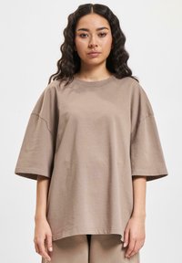 Brun oversized bomull t-skjorte med korte ermer, rund halslinje og avslappet passform; jevn tekstur, enkel design uten mønstre.