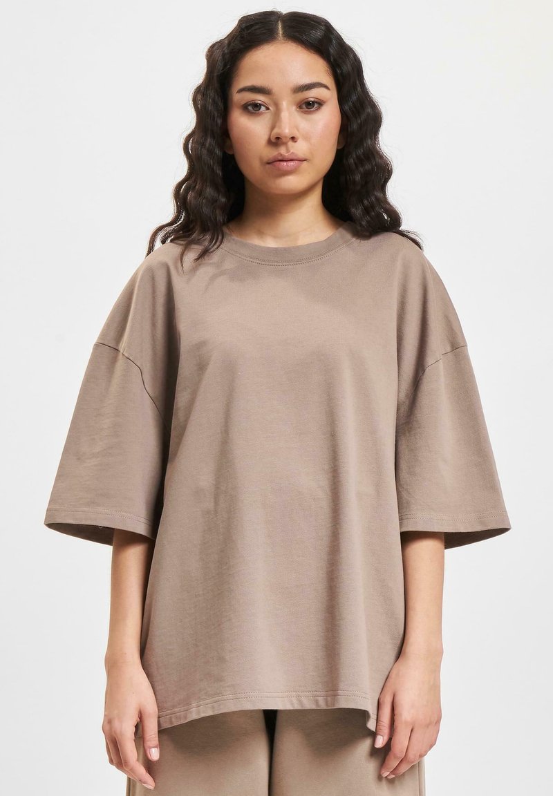Brun oversized bomull t-skjorte med korte ermer, rund halslinje og avslappet passform; jevn tekstur, enkel design uten mønstre.