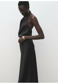 Haut noir à col licou en tissu lisse avec dos ouvert, associé à une jupe noire taille haute. Bracelet manchette métallique et boucles d'oreilles créoles.