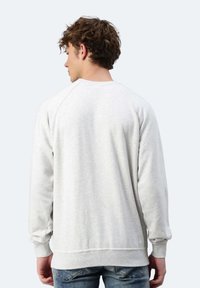 Felpa grigia con collo rotondo, maniche raglan, polsini e orlo a coste, realizzata in un tessuto morbido, presenta una texture liscia e un design semplice.